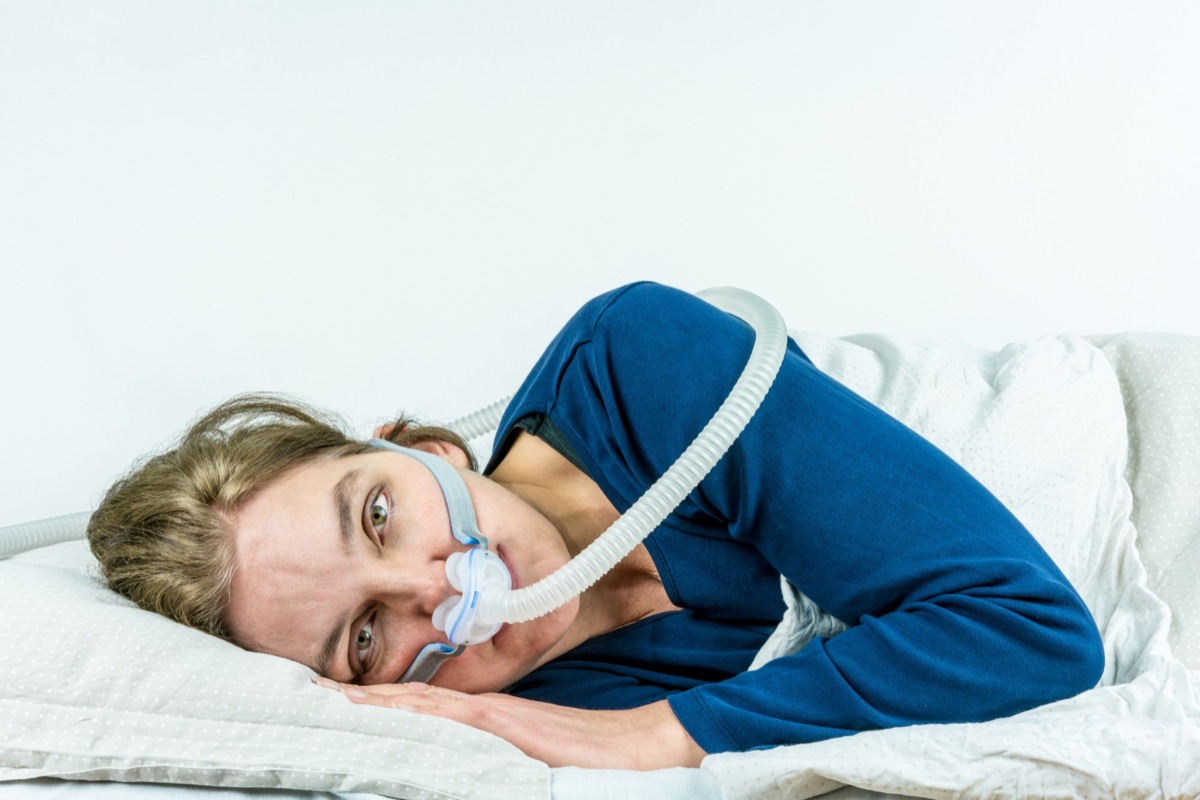 Woman lying awake in bed wearing a CPAP mask for sleep apnea